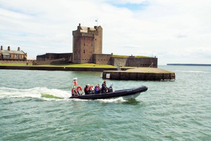 A boat with passengers passes a historic castle beside a calm sea.