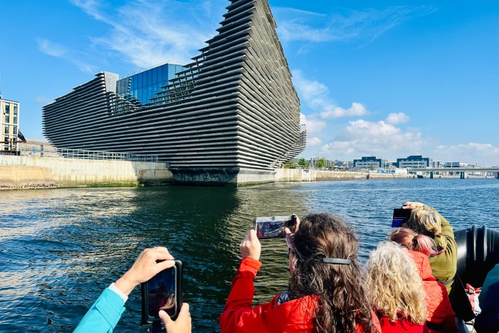 People on a boat photographing a modern, angular building by the water.