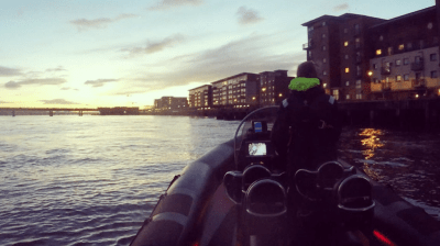 Person on a boat at dusk with city buildings along the waterfront.