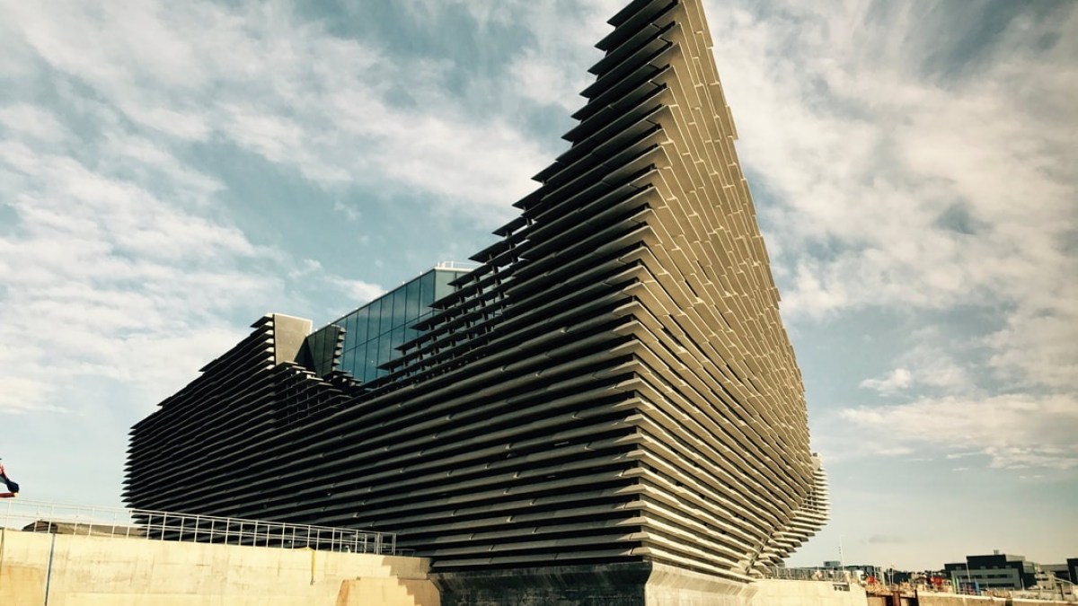 Modern, angular building with layered facade by the waterfront under a partly cloudy sky.