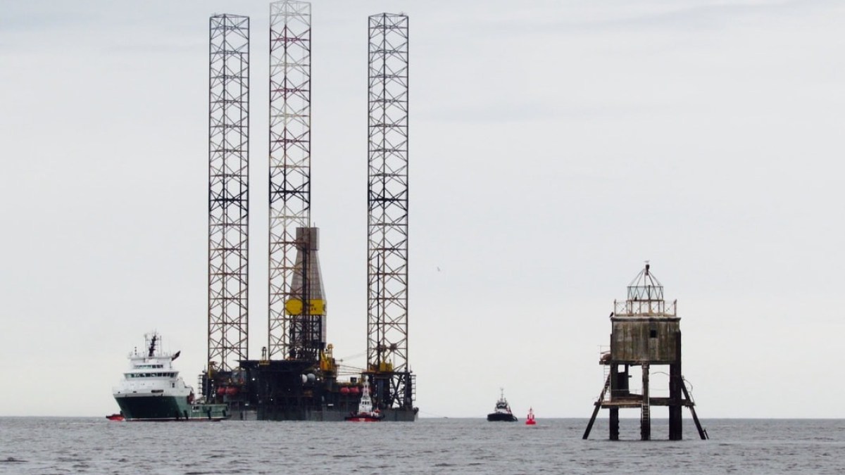 Offshore oil platform with support vessels and a small lighthouse structure in the sea.
