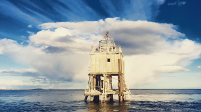 Wooden lighthouse on stilts in the ocean under a dramatic sky.