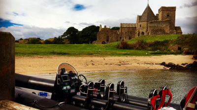 Inflatable boat docked by sandy shore with historic stone building in background.