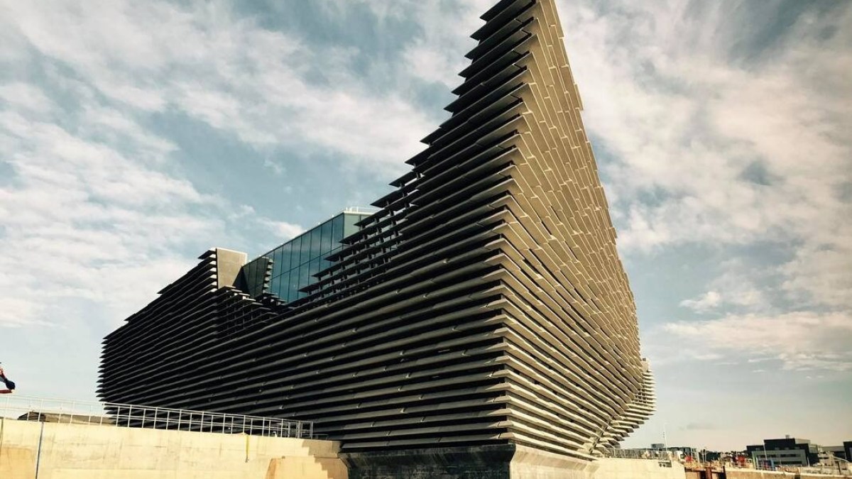 Angular modern building with tiered facade by a waterfront under a partly cloudy sky.