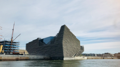 Modern building with layered design by water, sailboat nearby.