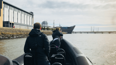 People on a boat near modern buildings and water in daylight.