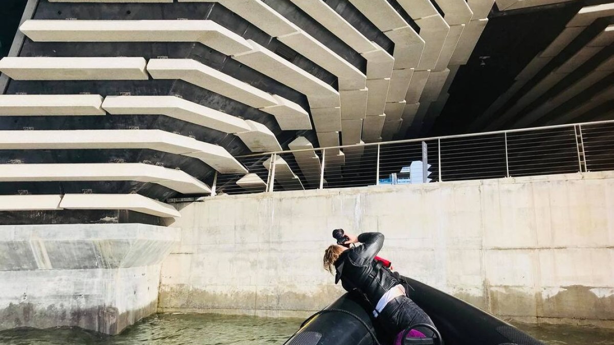 Person in a boat photographing a modern, geometric concrete structure from below.