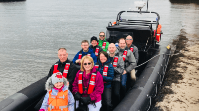 Group of people in life jackets on a boat near a shore.