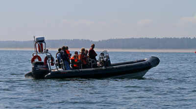 Boat with multiple people in life jackets on a calm sea with distant shoreline.