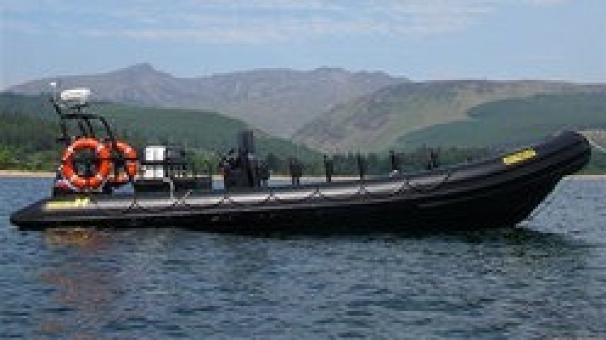 Black rigid inflatable boat on a lake with mountains in the background.