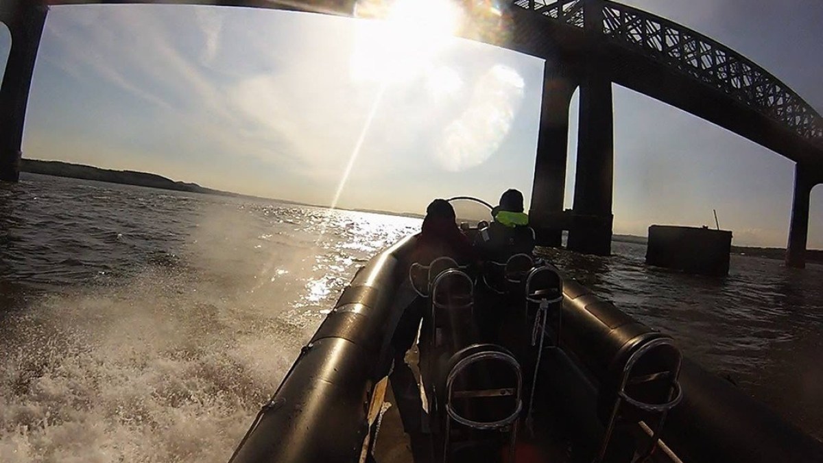 Boat under a bridge on sunny water with two people on board.